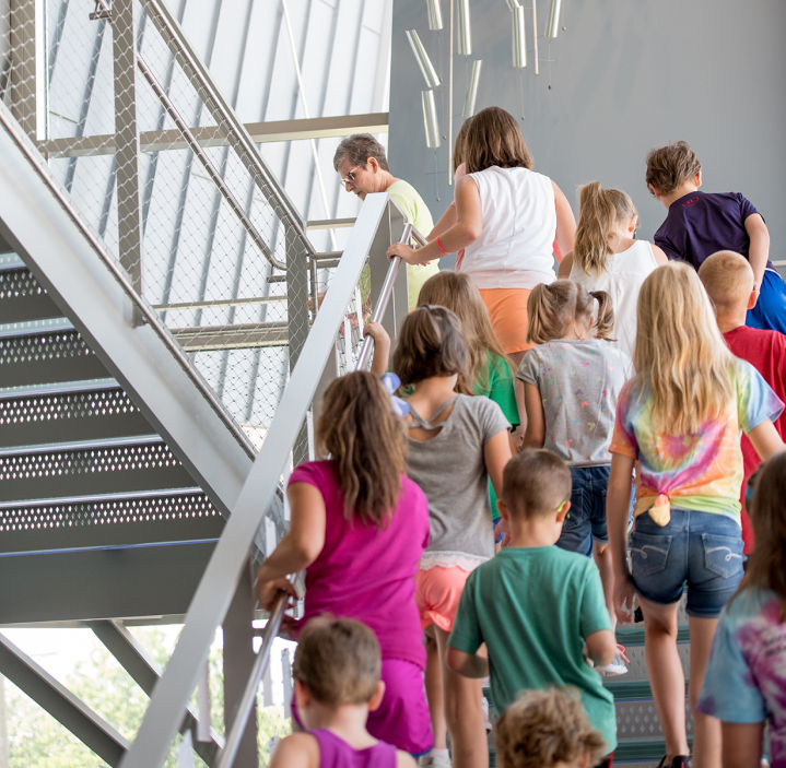 A group of elementary school children following a museum tour guide up a staircase towards The Westmoreland’s galleries.