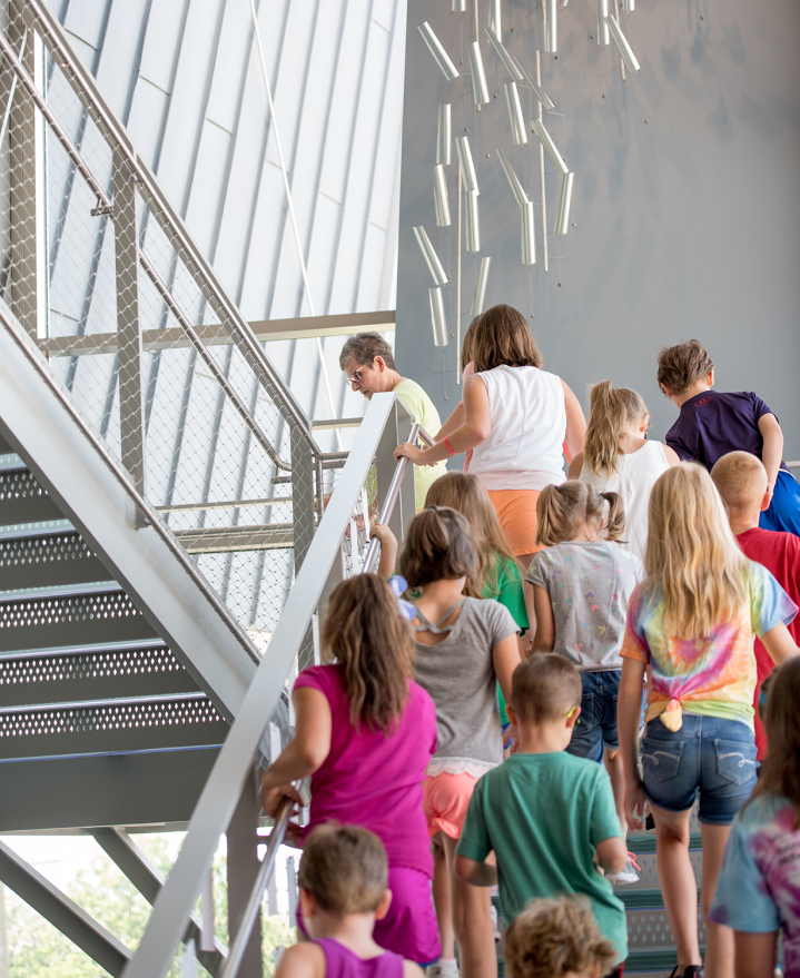 A group of elementary school children following a museum tour guide up a staircase towards The Westmoreland’s galleries.