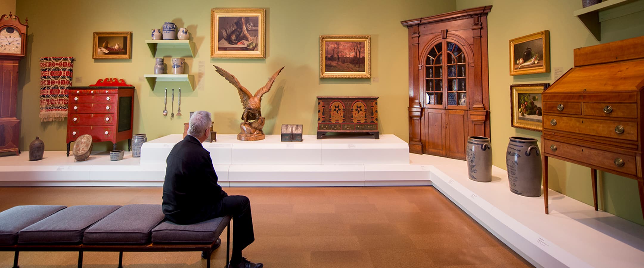 A visitor sitting on a bench while observing paintings, pieces of furniture, sculptures, and pottery in The Westmoreland’s 19th Century Gallery