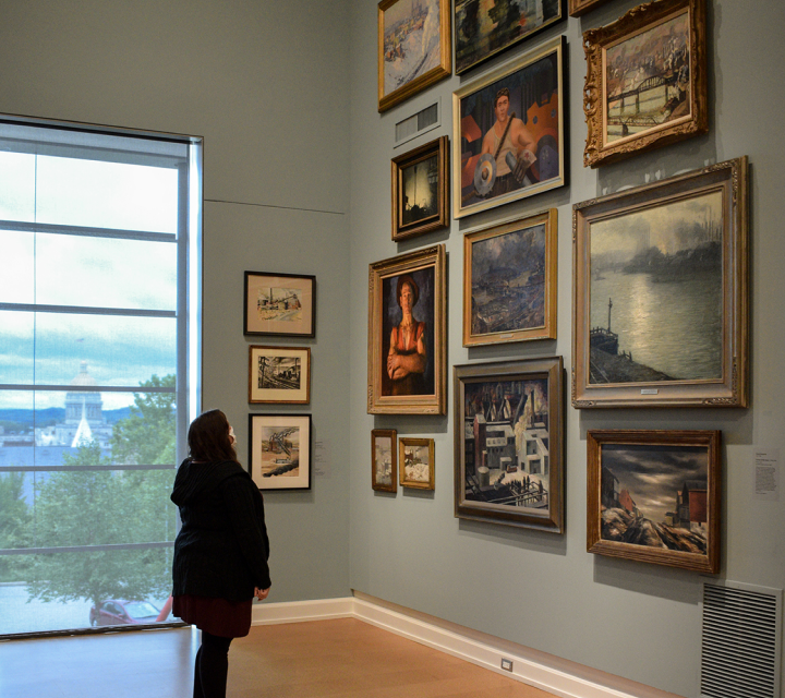 One visitor observing 20th Century paintings of Pittsburgh’s industrialized landscape in varying shapes and sizes hung salon style in the Westmoreland’s McKenna Gallery